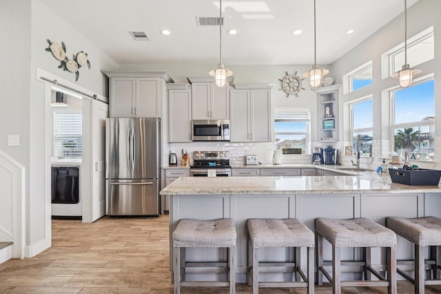 22212 Cantina Dr, Galveston, TX 77554 - kitchen featuring appliances with stainless steel finishes, a kitchen bar, light wood-style floors, a peninsula, and light stone countertops