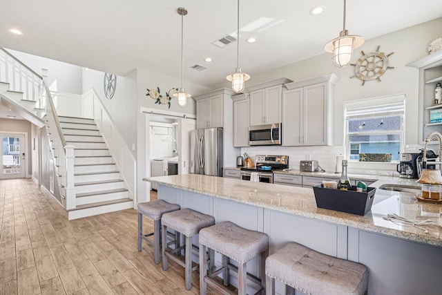 22212 Cantina Dr, Galveston, TX 77554 - kitchen featuring appliances with stainless steel finishes, a kitchen bar, light stone countertops, recessed lighting, and light wood-type flooring