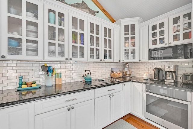 3906 Bridge Harbor Dr, Galveston, TX 77554 - kitchen featuring stainless steel oven, vaulted ceiling, backsplash, glass insert cabinets, and white cabinetry