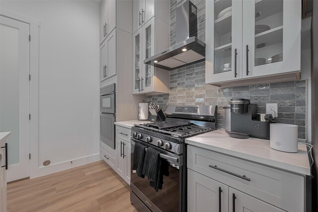 1305 E 27th St Unit A, Houston, TX 77009 - kitchen featuring wall chimney exhaust hood, range with gas cooktop, decorative backsplash, and stainless steel double oven