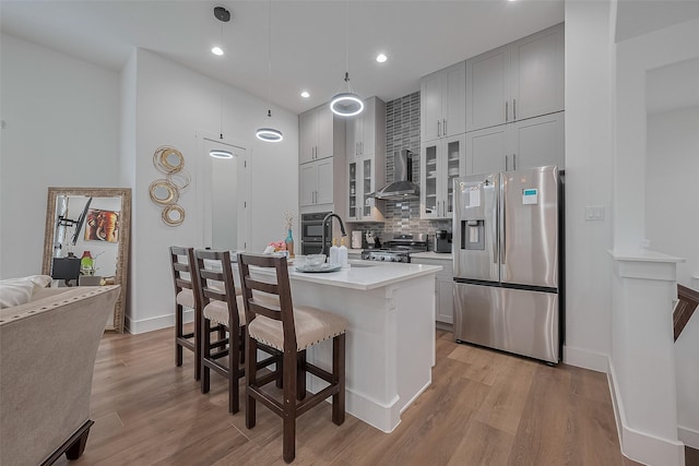 1305 E 27th St Unit A, Houston, TX 77009 - kitchen with appliances with stainless steel finishes, wall chimney range hood, decorative backsplash, a breakfast bar, and light wood-style floors
