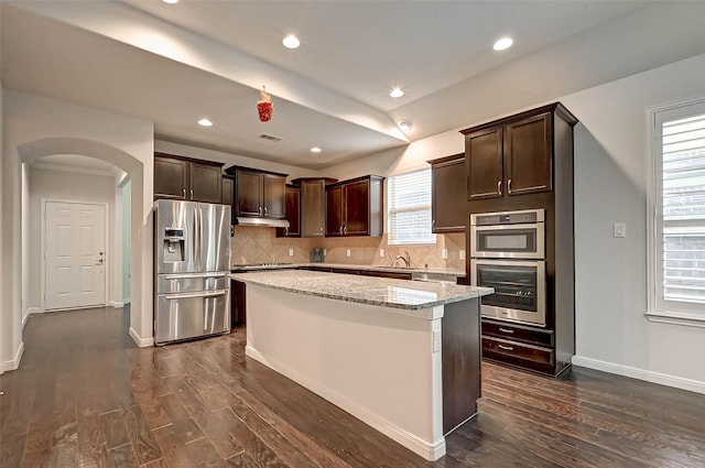 6438 Burgess Heights Ln, Katy, TX 77494 - kitchen with appliances with stainless steel finishes, dark brown cabinetry, arched walkways, backsplash, and dark wood-style flooring