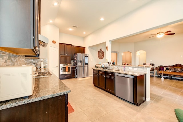 6119 Cresting Knolls Cir, Richmond, TX 77407 - kitchen featuring stainless steel appliances, arched walkways, open floor plan, ceiling fan, and light stone countertops