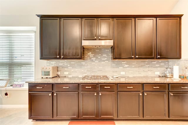 6119 Cresting Knolls Cir, Richmond, TX 77407 - kitchen with stainless steel gas stovetop, under cabinet range hood, decorative backsplash, and light stone counters