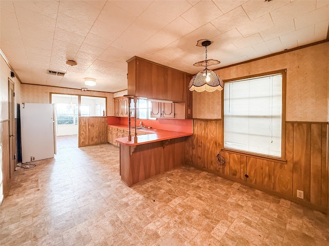 1002 Neiser Ln, Weimar, TX 78962 - kitchen with freestanding refrigerator, brown cabinetry, wooden walls, a peninsula, and a wainscoted wall