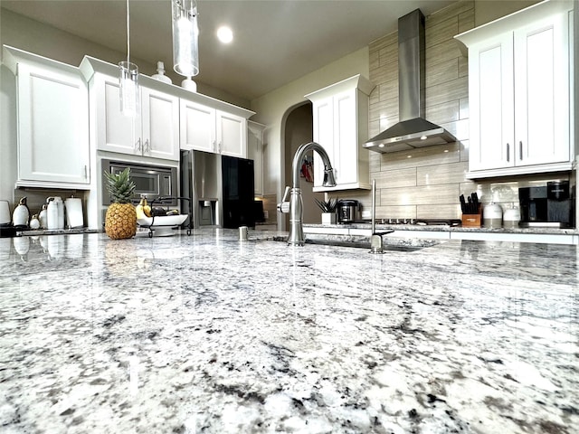 9723 Reston Ranch Ct, Cypress, TX 77433 - kitchen featuring wall chimney range hood, backsplash, appliances with stainless steel finishes, arched walkways, and light stone countertops