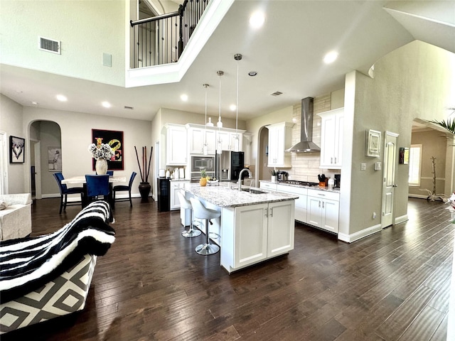 9723 Reston Ranch Ct, Cypress, TX 77433 - kitchen with wall chimney range hood, arched walkways, a towering ceiling, appliances with stainless steel finishes, and a breakfast bar area