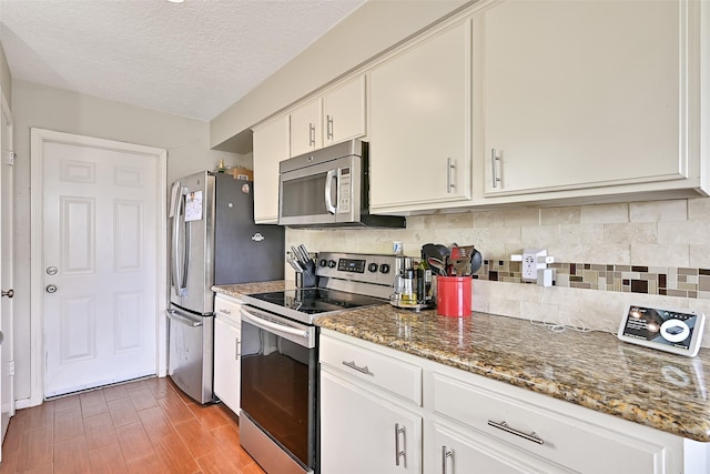 17202 Heritage Bay Dr, Webster, TX 77598 - kitchen featuring appliances with stainless steel finishes, backsplash, white cabinets, a textured ceiling, and dark stone countertops