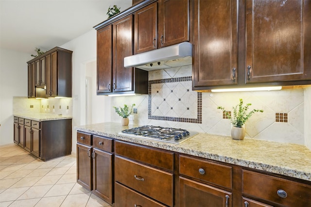 19014 Ridge Cove Ln, Cypress, TX 77433 - kitchen featuring under cabinet range hood, stainless steel gas cooktop, light stone countertops, backsplash, and light tile patterned floors