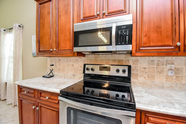 880 Swallow Dr, Palacios, TX 77465 - kitchen featuring stainless steel appliances, brown cabinets, tasteful backsplash, and light tile patterned floors