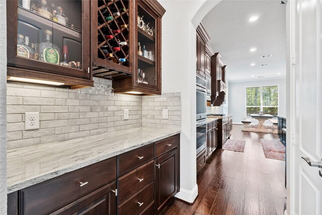 315 Lagarto Way, Pinehurst, TX 77362 - kitchen with dark brown cabinetry, arched walkways, dark wood-style flooring, glass insert cabinets, and light stone counters