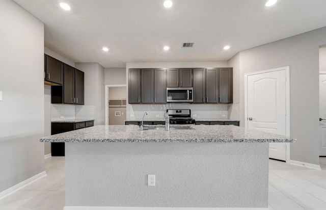 4827 Austin Meadow Ln, Katy, TX 77449 - kitchen with appliances with stainless steel finishes, tasteful backsplash, light stone counters, an island with sink, and recessed lighting