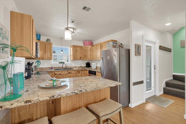 123 Howard Ave, Surfside Beach, TX 77541 - kitchen featuring appliances with stainless steel finishes, a peninsula, a sink, light wood-type flooring, and light stone counters