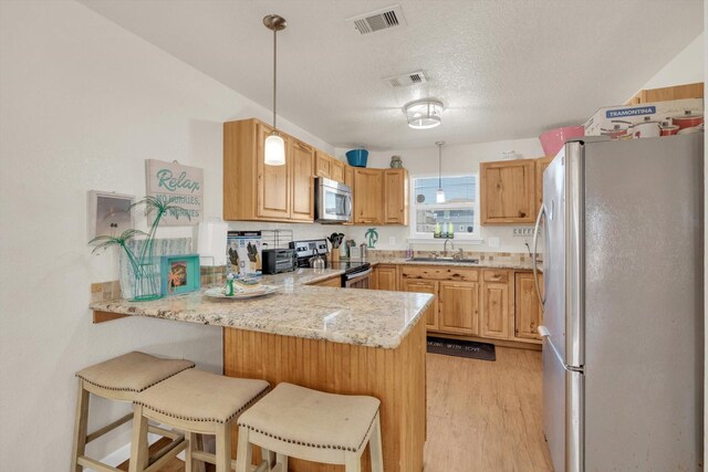123 Howard Ave, Surfside Beach, TX 77541 - kitchen featuring stainless steel appliances, a peninsula, a sink, light wood-style floors, and light stone countertops