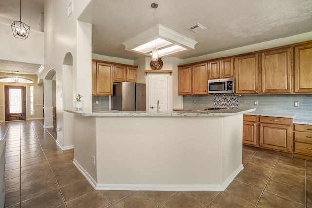 20918 Normandy Forest Dr, Spring, TX 77388 - kitchen with appliances with stainless steel finishes, dark tile patterned floors, arched walkways, backsplash, and brown cabinets