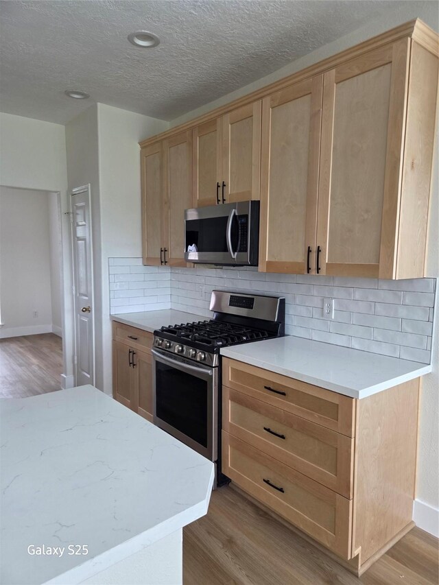 16111 Aberdeen Forest Dr, Houston, TX 77095 - kitchen with appliances with stainless steel finishes, light brown cabinets, light wood finished floors, backsplash, and a textured ceiling