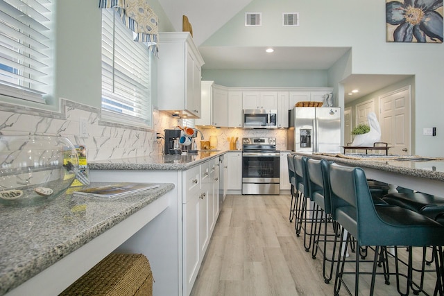 1214 Hwy 87, Gilchrist, TX 77617 - kitchen featuring appliances with stainless steel finishes, white cabinets, light wood finished floors, light stone countertops, and tasteful backsplash