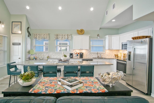 1214 Hwy 87, Gilchrist, TX 77617 - kitchen with stainless steel appliances, a sink, white cabinets, decorative backsplash, and lofted ceiling
