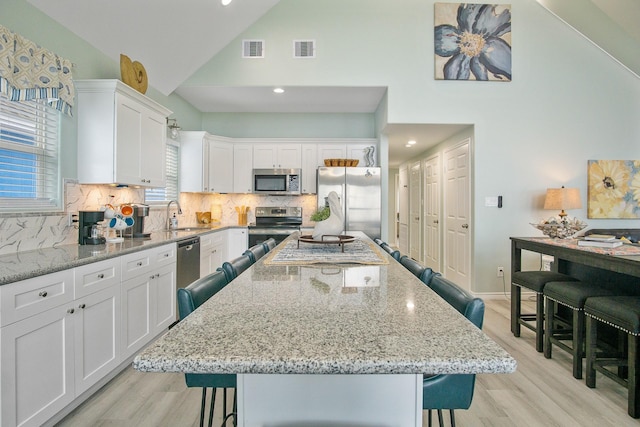1214 Hwy 87, Gilchrist, TX 77617 - kitchen featuring stainless steel appliances, a kitchen bar, high vaulted ceiling, white cabinets, and a kitchen island