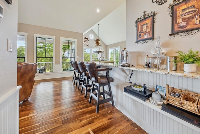 1932 Chappell Ridge Ln, Chappell Hill, TX 77426 - kitchen with wood finished floors, light stone countertops, a kitchen breakfast bar, a wainscoted wall, and high vaulted ceiling