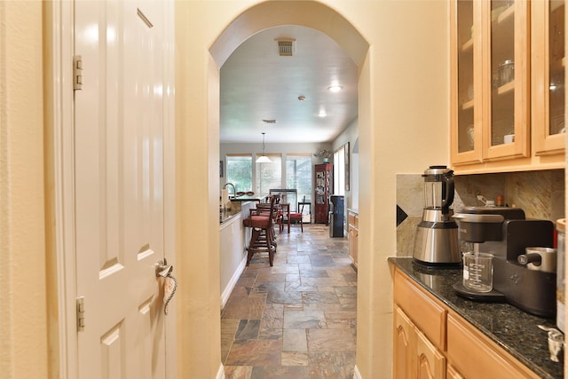 2107 N Shadow Grove Ln, Richmond, TX 77406 - kitchen featuring stone tile floors, arched walkways, glass insert cabinets, dark stone countertops, and light brown cabinets