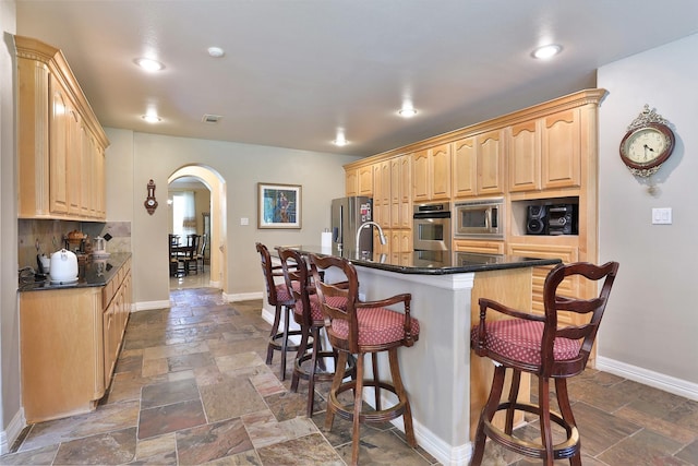 2107 N Shadow Grove Ln, Richmond, TX 77406 - kitchen featuring stainless steel appliances, arched walkways, light brown cabinets, stone tile flooring, and a kitchen breakfast bar