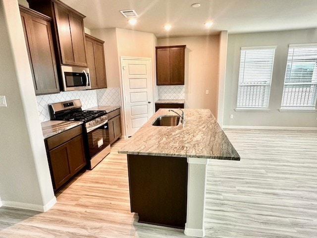 27207 Blue Pool Dr, Katy, TX 77493 - kitchen with appliances with stainless steel finishes, a sink, light wood-style floors, a kitchen island with sink, and baseboards