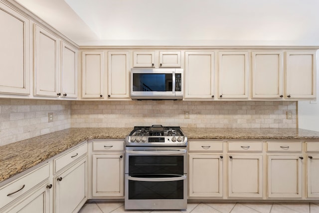 38 Florian Ct, Conroe, TX 77385 - kitchen with range with two ovens, cream cabinetry, tasteful backsplash, light tile patterned floors, and light stone countertops