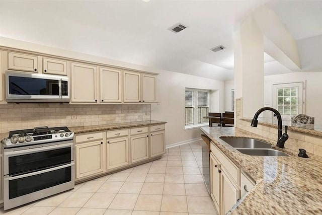 38 Florian Ct, Conroe, TX 77385 - kitchen with stainless steel appliances, cream cabinetry, a sink, decorative backsplash, and light stone counters