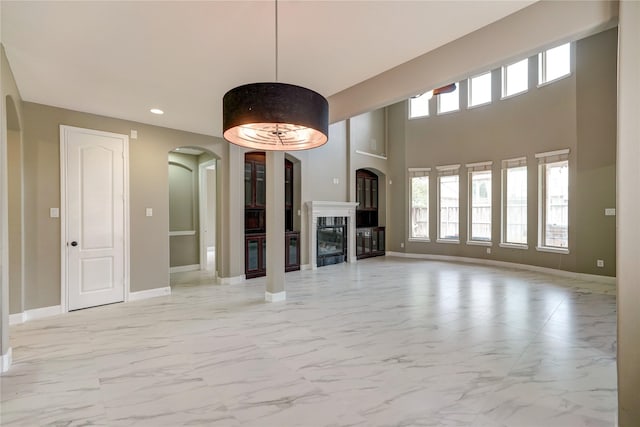 17215 Astrachan Rd, Richmond, TX 77407 - unfurnished living room featuring arched walkways, light marble finish floors, a glass covered fireplace, baseboards, and recessed lighting