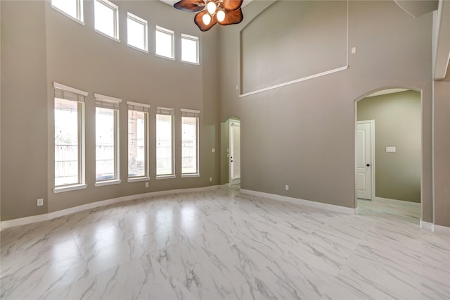 17215 Astrachan Rd, Richmond, TX 77407 - unfurnished living room with ceiling fan, arched walkways, marble finish floors, a towering ceiling, and baseboards