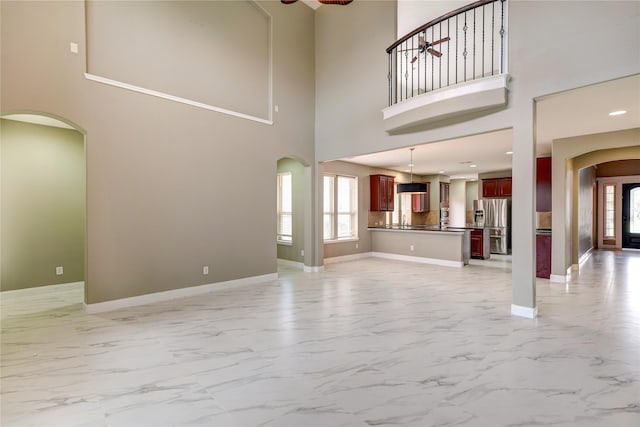 17215 Astrachan Rd, Richmond, TX 77407 - unfurnished living room featuring arched walkways, light marble finish flooring, plenty of natural light, and a towering ceiling