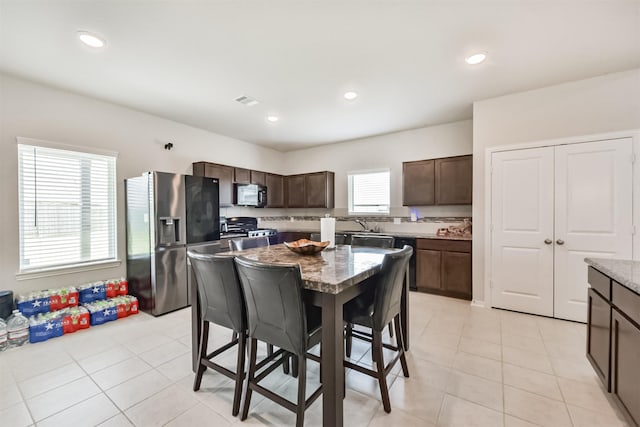 3607 Crosspointe Pass, Angleton, TX 77515 - kitchen with appliances with stainless steel finishes, a kitchen bar, dark brown cabinets, light tile patterned floors, and a kitchen island