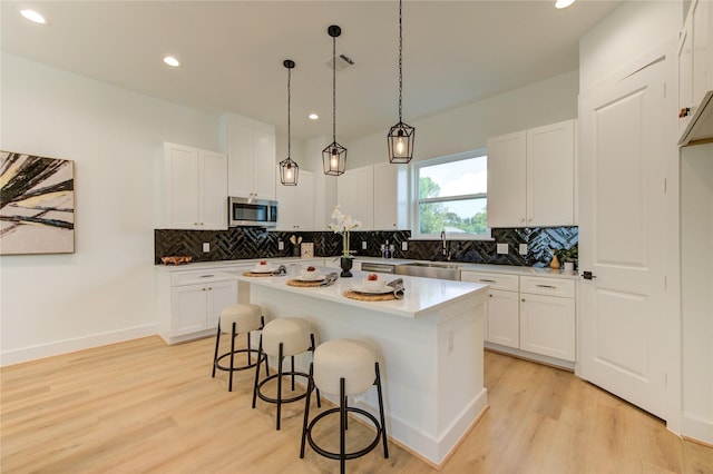 4043 Buck St, Houston, TX 77020 - kitchen with stainless steel microwave, light wood-type flooring, a breakfast bar, backsplash, and recessed lighting
