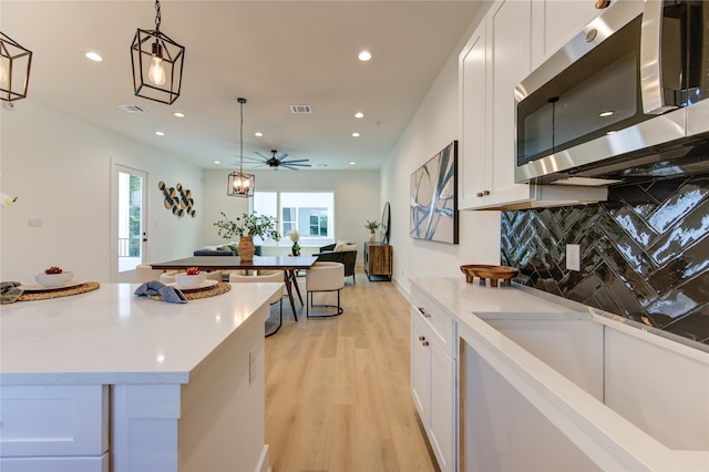 4043 Buck St, Houston, TX 77020 - kitchen with stainless steel microwave, backsplash, white cabinets, light wood-style floors, and hanging light fixtures