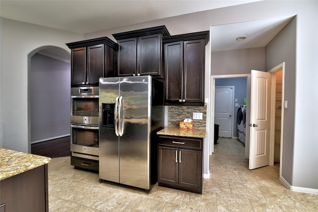 24302 Marisa Ln, Richmond, TX 77406 - kitchen featuring stainless steel appliances, separate washer and dryer, light stone counters, arched walkways, and backsplash