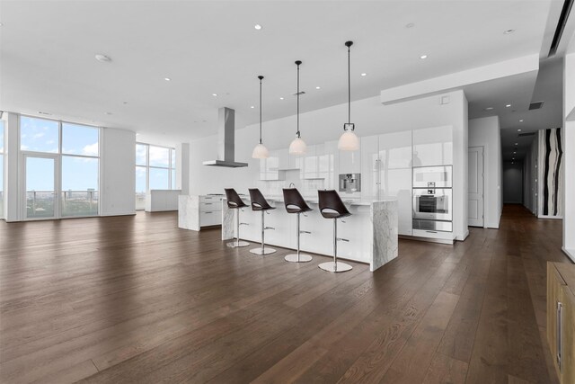 4521 San Felipe St Unit 3101, Houston, TX 77027 - kitchen featuring wall chimney range hood, a breakfast bar, white cabinets, dark wood-style floors, and a large island with sink