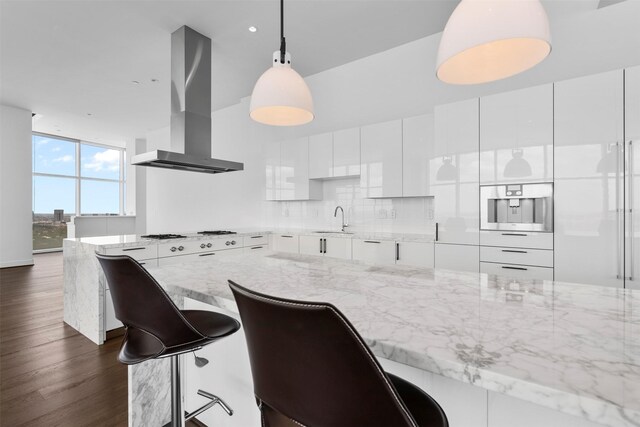 4521 San Felipe St Unit 3101, Houston, TX 77027 - kitchen with wall chimney exhaust hood, white cooktop, white cabinets, dark wood-type flooring, and light stone counters