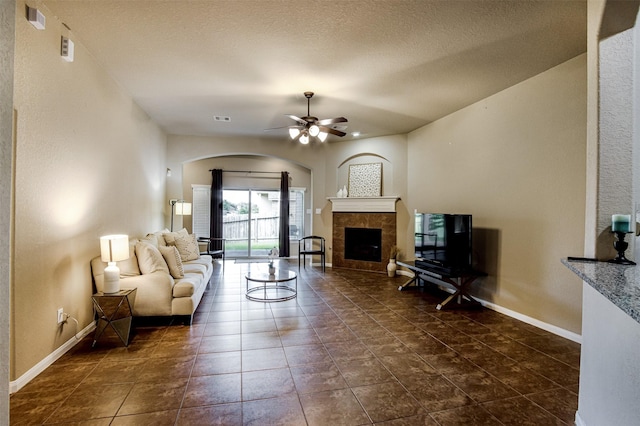 2039 Wembley Way, Rosenberg, TX 77471 - living area with a tiled fireplace, a ceiling fan, arched walkways, baseboards, and dark tile patterned floors