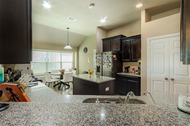 2039 Wembley Way, Rosenberg, TX 77471 - kitchen with stainless steel fridge, a sink, light stone counters, dark brown cabinetry, and decorative light fixtures