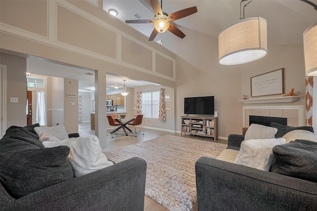 21415 Park Timbers Ln, Katy, TX 77450 - living room featuring light wood-style flooring, ceiling fan, a fireplace, a towering ceiling, and baseboards