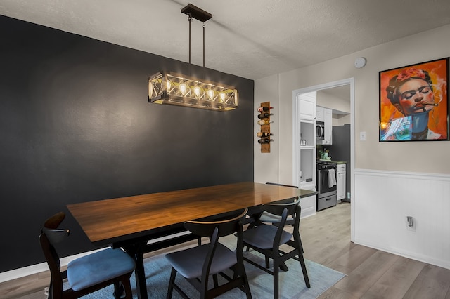 12250 Beamer Rd, Houston, TX 77089 - dining area with light wood-style floors, a chandelier, a textured ceiling, and a wainscoted wall