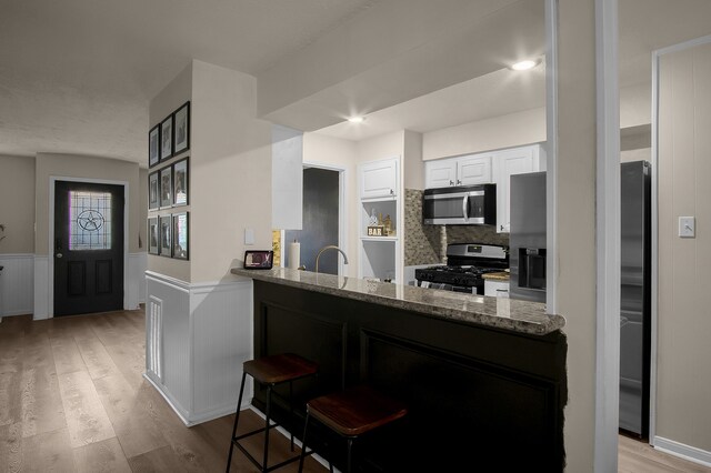 12250 Beamer Rd, Houston, TX 77089 - kitchen with appliances with stainless steel finishes, white cabinetry, light wood finished floors, a wainscoted wall, and light stone counters