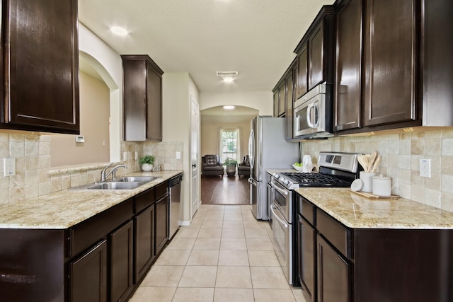 9115 E Lakeside Dr, Magnolia, TX 77354 - kitchen featuring stainless steel appliances, arched walkways, dark brown cabinets, light tile patterned flooring, and a sink