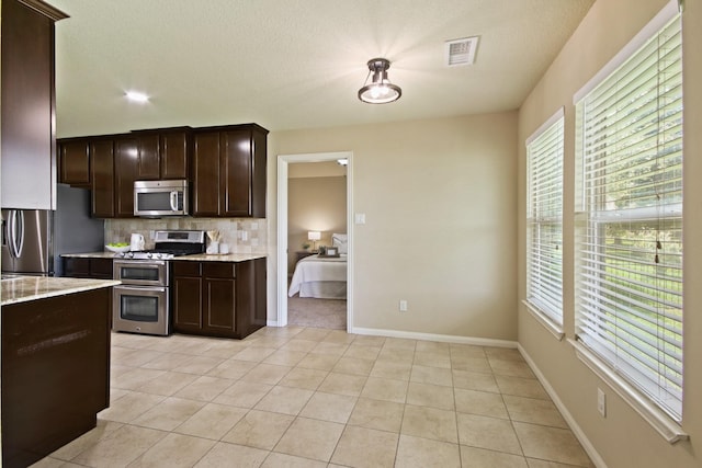 9115 E Lakeside Dr, Magnolia, TX 77354 - kitchen with appliances with stainless steel finishes, dark brown cabinetry, decorative backsplash, plenty of natural light, and a textured ceiling