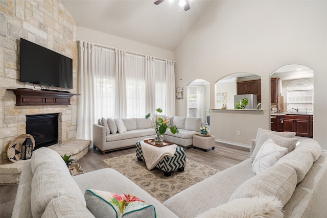 2106 Asbury Ct, Pearland, TX 77581 - living area with a ceiling fan, light wood-style flooring, high vaulted ceiling, a stone fireplace, and arched walkways