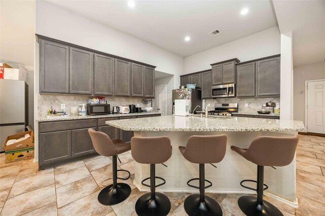 4507 Terrazza Verde Dr, Katy, TX 77493 - kitchen with stainless steel appliances, decorative backsplash, a kitchen bar, an island with sink, and light stone counters
