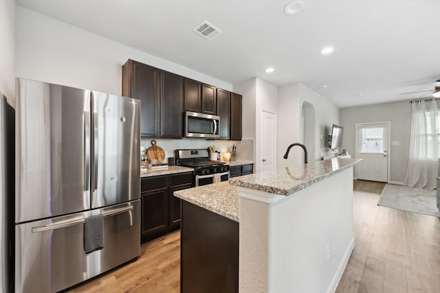 2037 Muggy Ln, Conroe, TX 77301 - kitchen with stainless steel appliances, dark brown cabinets, light stone counters, a kitchen island with sink, and light wood-type flooring