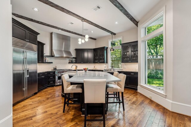 6014 Floyd St, Houston, TX 77007 - kitchen featuring premium appliances, wall chimney range hood, beam ceiling, healthy amount of natural light, and an island with sink