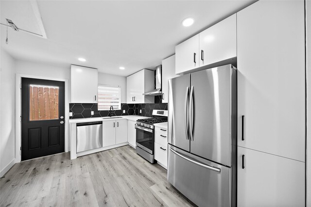 1106 W Tri Oaks Ln Unit 134, Houston, TX 77043 - kitchen with appliances with stainless steel finishes, wall chimney exhaust hood, light wood-style flooring, white cabinetry, and decorative backsplash